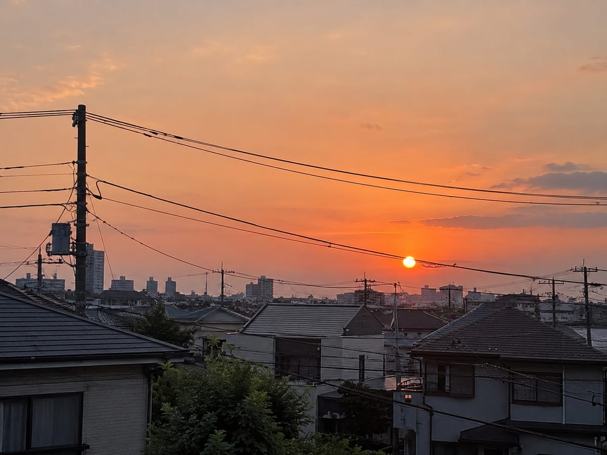 住宅街の屋根と電線の向こうに広がる夕空